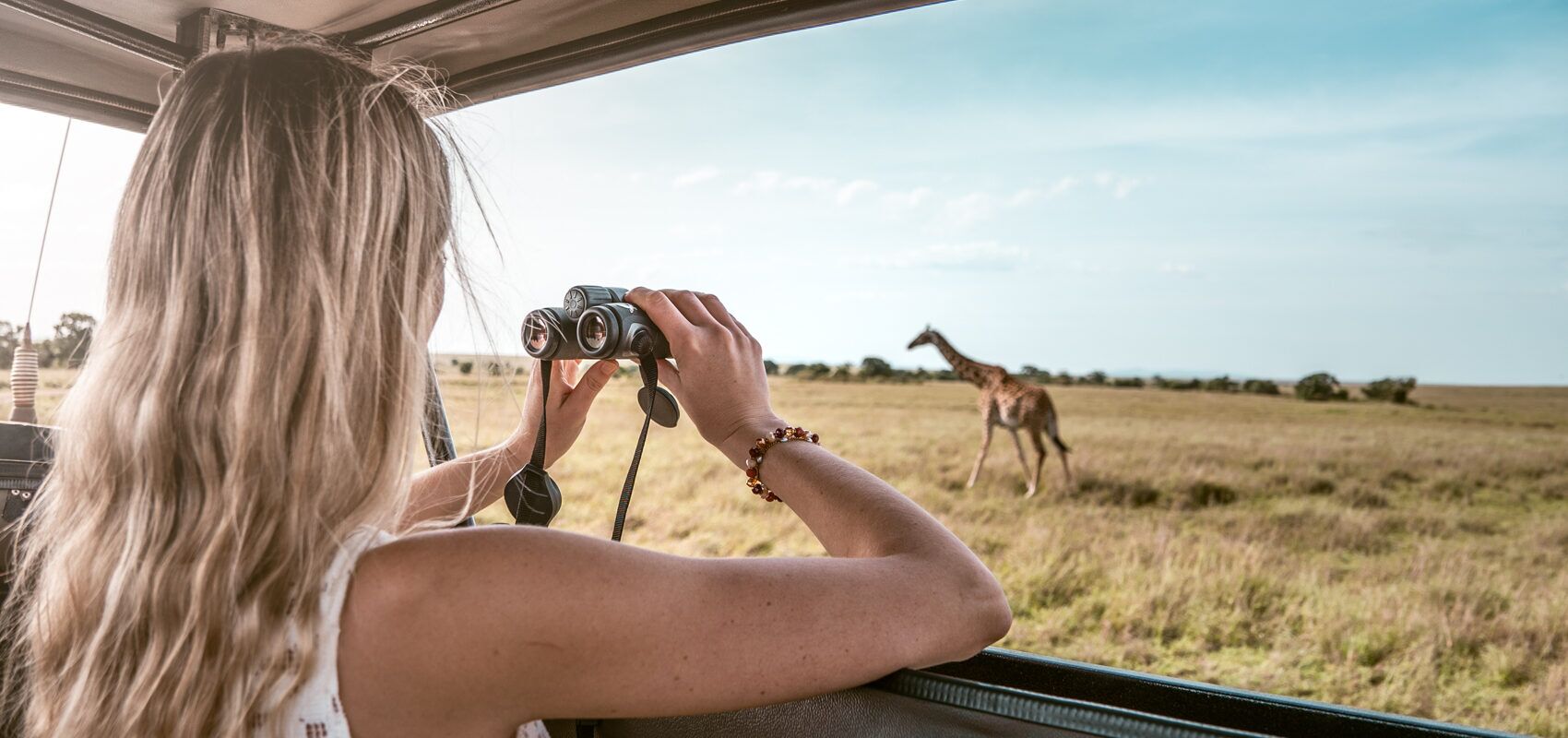 Un voyage au Kenya, ou l'aventure ultime. Une femme observe une girafe dans la savane avec des jumelles.